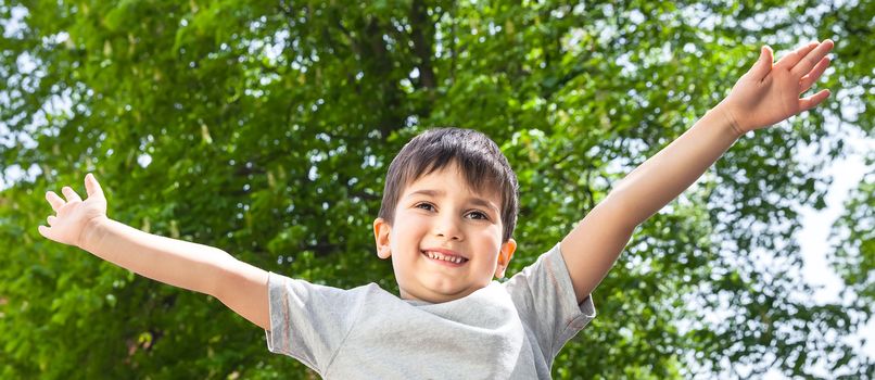 Happy boy with his hands up smiling on green tree background