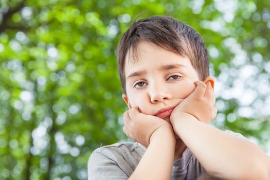 Sad little boy looking at something against blurred natural background