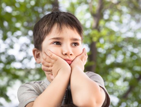 Sad little boy looking at something against blurred natural background