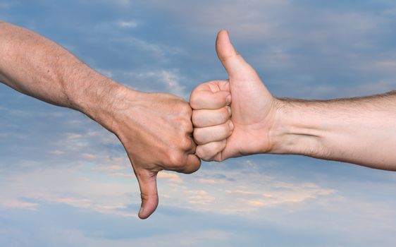 Clash of the thumbs up and thumbs down hand signs against of the cloudy sky