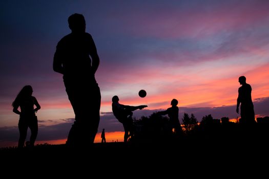 Night scene. Silhouettes of young people playing with a ball on the sunset sky background
