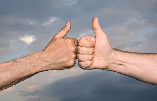 Friendship concept. Two men bumping fists with thumbs up against sky with clouds