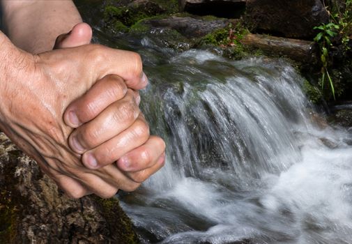 An elderly man washes his hands in a forest creek