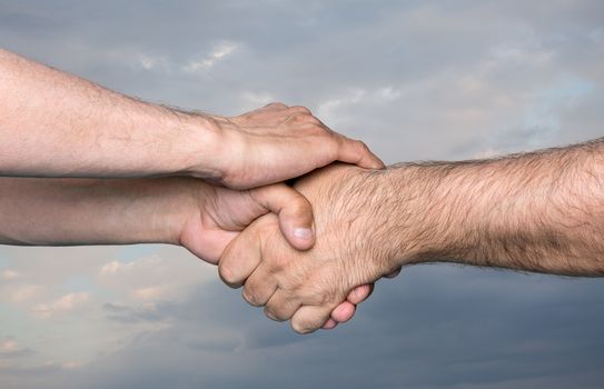 Handshaking. Shaking hands of two male people against the sky with thunder clouds