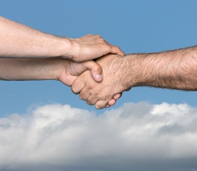 Handshaking. Shaking hands of two male people against the sky with clouds