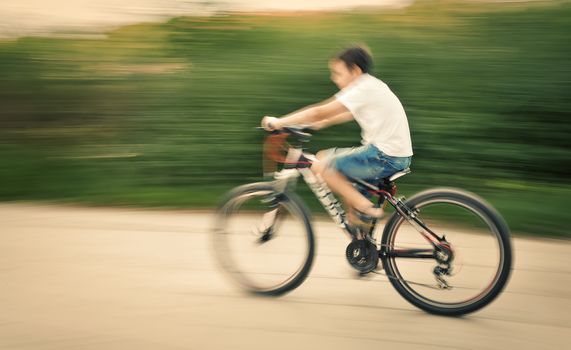 Boy cyclist in traffic on the city roadway. Intentional motion blur and color shift