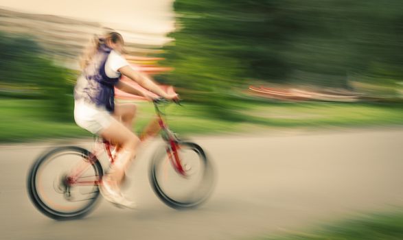 Girl cyclist in traffic on the city roadway. Intentional motion blur and color shift