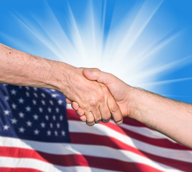 The USA flag and shaking hands of two male people on blue sky background