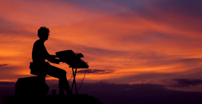 Silhouette of musician playing the electric piano on the sunset sky background