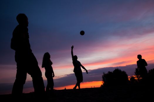 Night scene. Silhouettes of young people playing with a ball on the sunset sky background