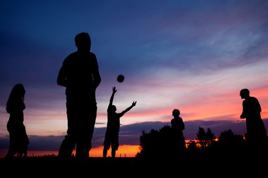 Night scene. Silhouettes of young people playing with a ball on the sunset sky background