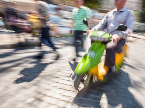 Old biker with a motorcycle in motion blur on city road in sunny day