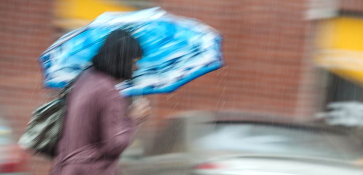 Rainfall in the city. Woman walking down the street in rainy day. Intentional motion blur