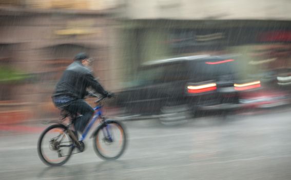 Rainfall in the city. Wet cyclist rides through the streets on a rainy day. Intentional motion blur