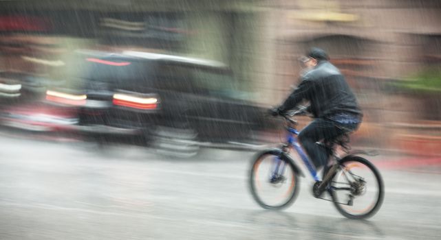 Rainfall in the city. Wet cyclist rides through the streets on a rainy day. Intentional motion blur