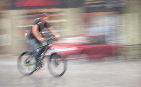 Rainfall in the city. Wet cyclist rides through the streets on a rainy day . Intentional motion blur