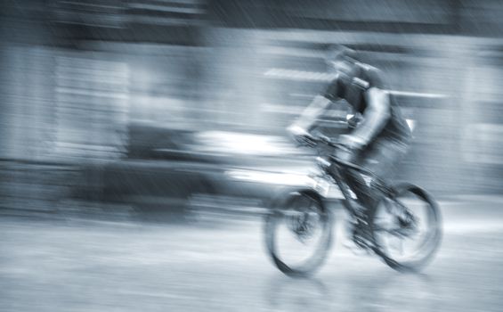 Rainfall in the city. Wet cyclist rides through the streets on a rainy day . Intentional motion blur