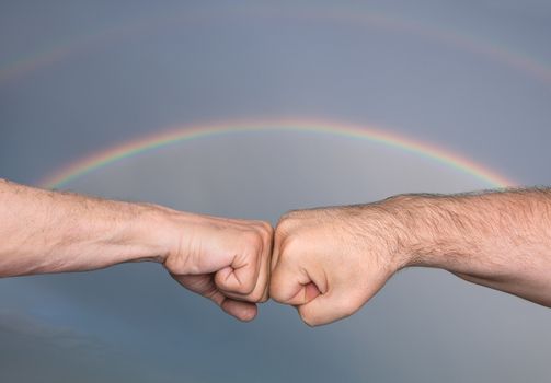 Two men bumping fists against the background of a stormy sky with rainbow