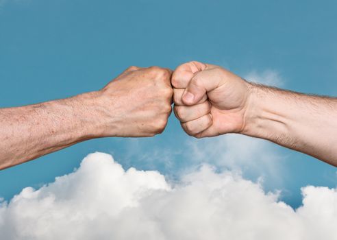 Two men bumping fists against the blue sky with white clouds