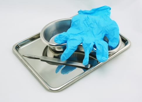 Medical devices include operation knife, emesis basin tray and glove resting on a white background.                               