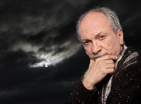 Portrait of an elderly man with a serious expression on a dark sky background