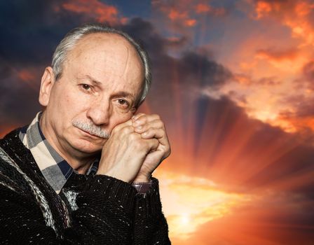 Handsome senior man with a skeptical expression on sunset sky background