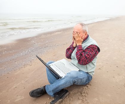 Problems. Old man sitting with notebook on beach.