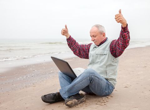 Success. Senior businessman sitting with notebook on beach on a foggy day