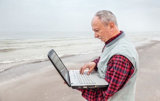 old man standing on the beach with a laptop on a foggy day