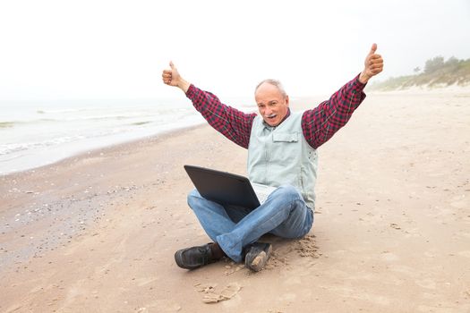 Happy old man on the beach with a laptop on a foggy day