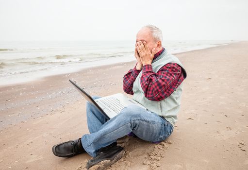 Fatigue. Old man sitting with notebook on beach on a foggy day