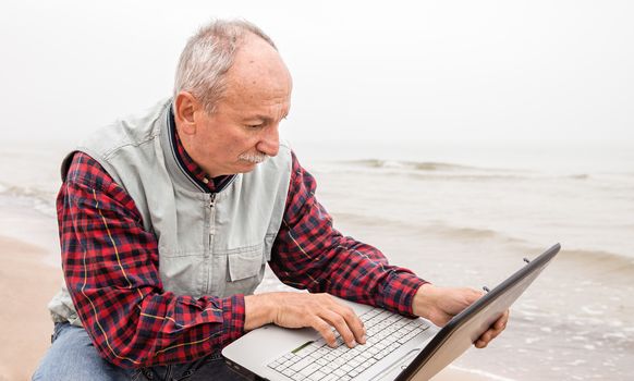 Old man on the beach with a laptop on a foggy day