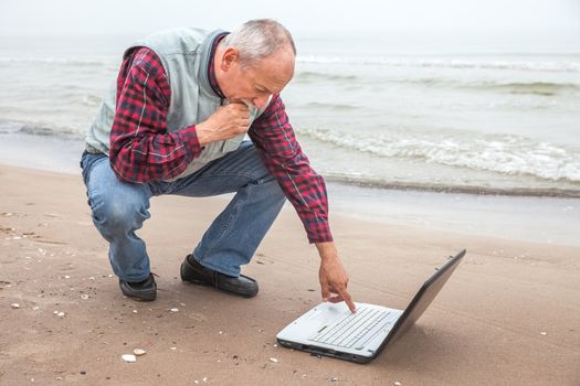 Elderly man working with a notebook on the beach against sea background 