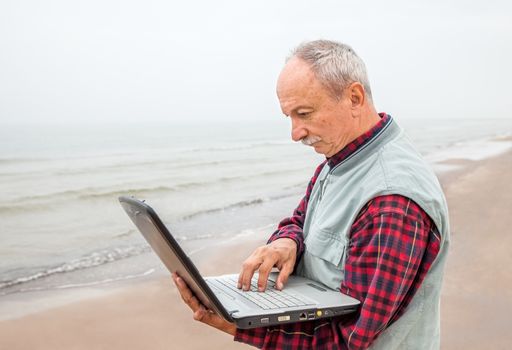 old man standing on the beach with a laptop on a foggy day