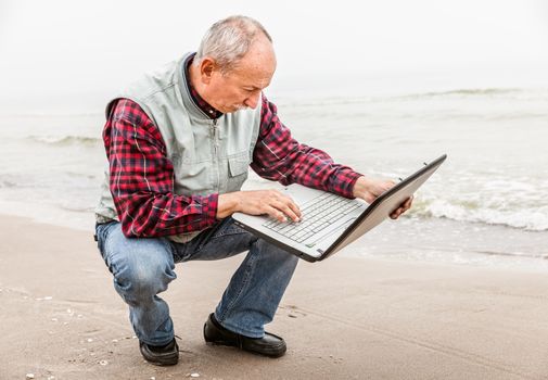 Old man sitting with notebook on beach.