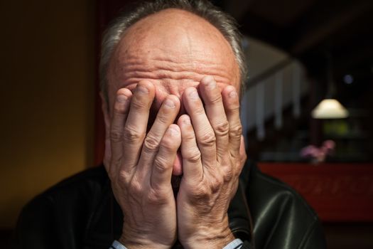 Depression. Elderly man sitting in the cafe. Covers his face by hand