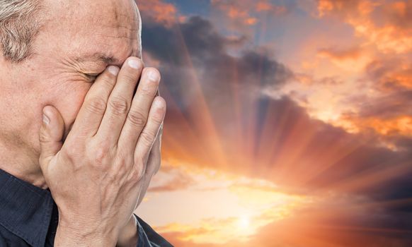 End of life's journey. Portrait of an elderly man with face closed by hand on sunset background