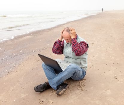 Problems. Senior businessman sitting with notebook on beach