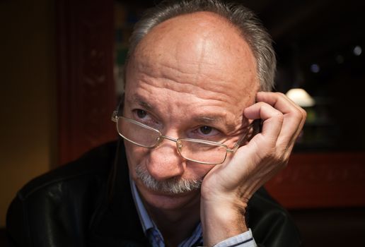 Portrait of a tired old man with glasses waiting for coffee at a cafe