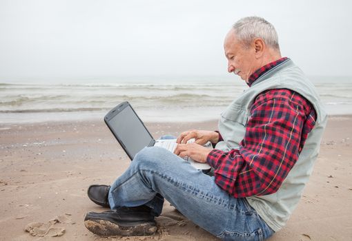 Elderly man working on a computer while sitting on the beach on a foggy day