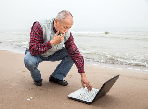 Elderly man working with a laptop on the beach