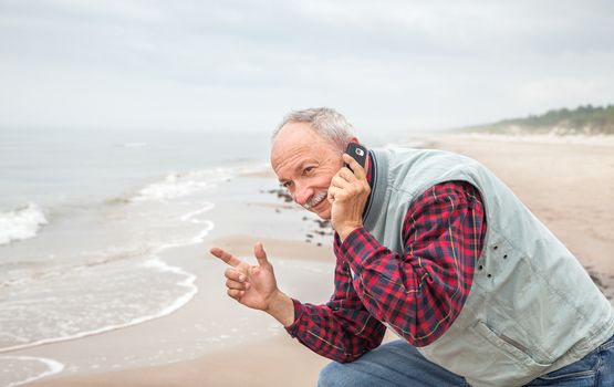 Portrait of an old senior man with a telephone on sea background