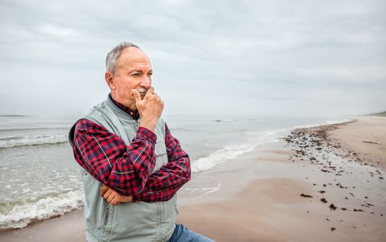 Thoughtful elderly man standing on the beach on a foggy day