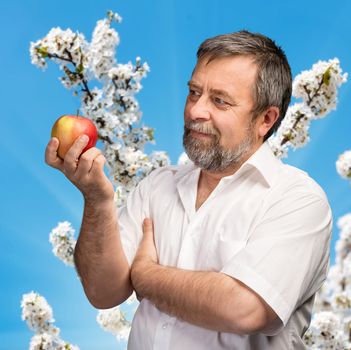 Handsome middle-aged man with red apple against of a blooming garden