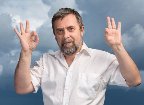 Successful man shows ok sigh on cloudy sky background