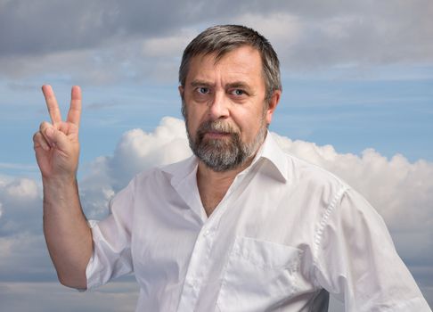 Middle-aged man in a white shirt showing victory sign on background of cloudy sky