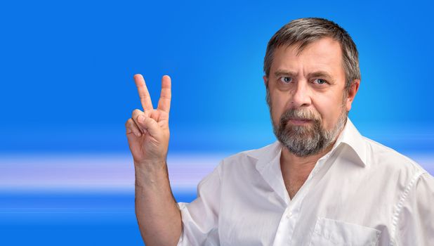 Middle-aged man in a white shirt showing victory sign on abstract blue background