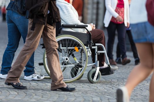 Close up of  woman on a wheelchair with a helper during walk in the busy street.