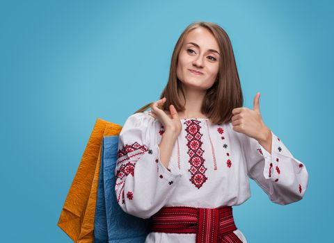 Happy girl in the Ukrainian national dress and shopping bags showing thumbs up