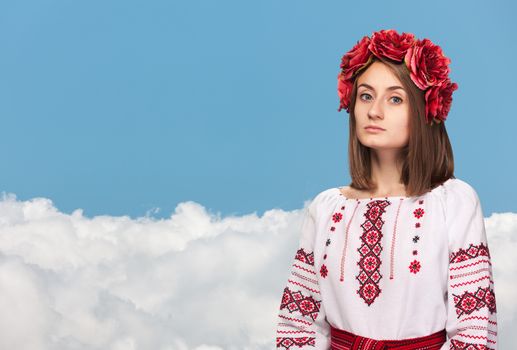 Beautiful sad girl in the Ukrainian national suit against the blue sky with white clouds